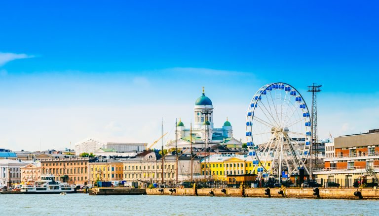 Helsingin rantaviiva kesäisenä iltana, tuomiokirkko ja vaaleanpunainen suurpyörä sinistä taivasta vasten.